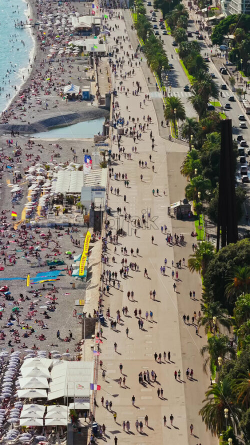 Video - Aerial drone view of crowded Nice beach with people sunbathing on pebbles and swimming in turquoise Mediterranean waters. Vertical, Nice, France