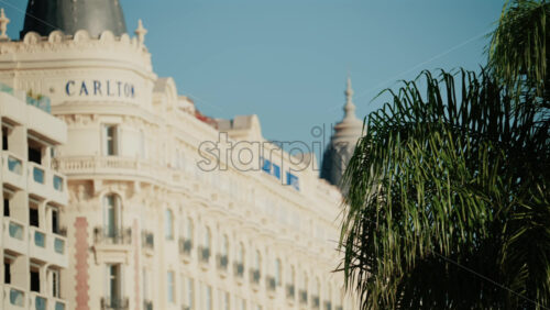 Video - Cannes, France - October 3, 2025: Blurred view of the Carlton Hotel facade with palm trees in the foreground under a clear blue sky