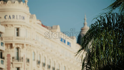 Video - Cannes, France - October 3, 2025: Blurred view of the Carlton Hotel facade with palm trees in the foreground under a clear blue sky