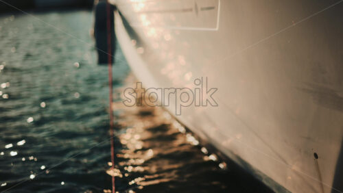 Video - Golden sunlight shimmering on the side of a yacht floating on calm water