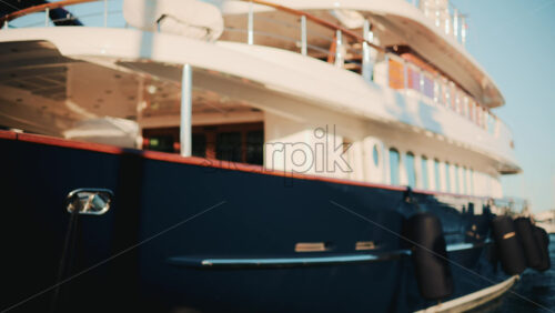 Video - Side view of a dark blue luxury yacht with chrome details and wooden deck, floating in a marina under bright sunlight