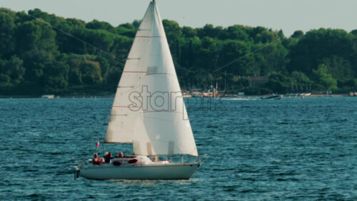 Video - White sailboat gliding across calm blue water near a green coastline