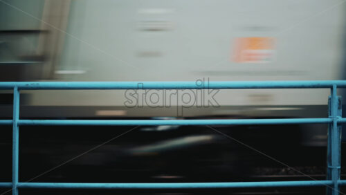 Video - Blurred motion of a train passing behind a blue metal fence with soft background colors
