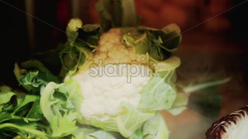 Video - Close up of a fresh cauliflower surrounded by green leaves under warm light