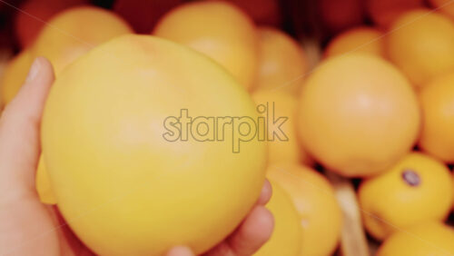 Video - Close up of a hand holding a bright orange fruit in a market