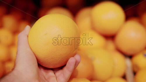 Video - Close up of a hand holding a bright orange fruit in a market