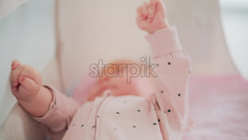 Video - Adorable baby resting in a cozy bed under natural light, wearing pastel pink pajamas