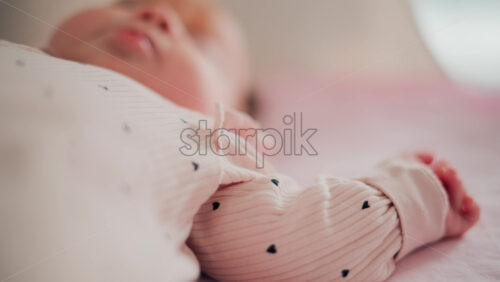 Video - Adorable baby resting in a cozy bed under natural light, wearing pastel pink pajamas