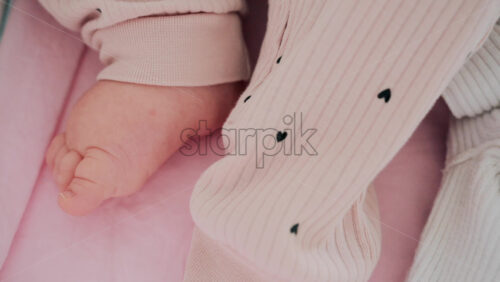 Video - Close up shot of a baby's feet resting on a bed, wearing soft pink clothes with small heart patterns