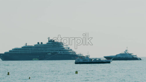 Video - Large cruise ship and luxury yachts anchored on calm blue sea under hazy sky