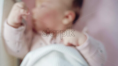 Video - Close up of a baby lying on a soft blanket, wearing a pastel pink outfit