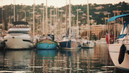Video - Elegant sailboats lined up in a marina during golden hour, calm water reflecting the evening sun