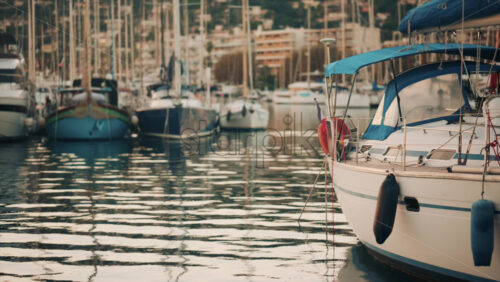 Video - Elegant sailboats lined up in a marina during golden hour, calm water reflecting the evening sun