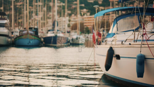 Video - Elegant sailboats lined up in a marina during golden hour, calm water reflecting the evening sun