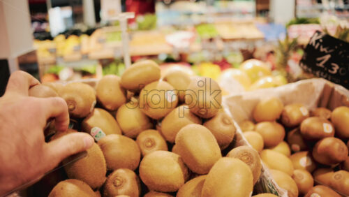 Video - Close up of a person selecting fresh kiwi fruit from a pile in a supermarket