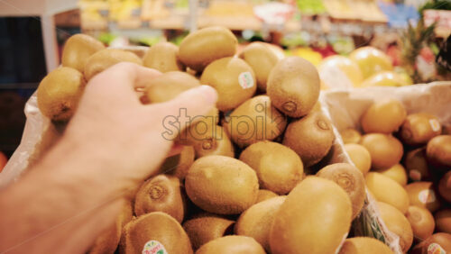 Video - Close up of a person selecting fresh kiwi fruit from a pile in a supermarket
