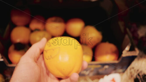 Video - Hand holding a persimmon with a Halloween style jack o' lantern face drawn on it in a grocery store