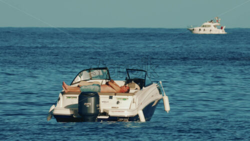 Video - Cannes, France - October 16, 2025: Man lying shirtless on a motorboat floating on calm blue water under sunlight