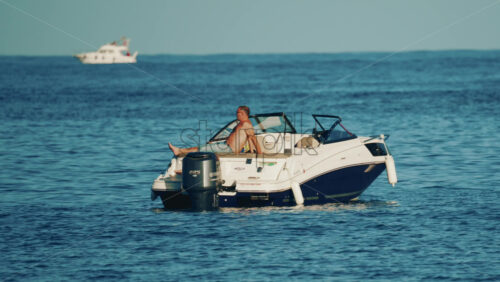 Video - Cannes, France - October 16, 2025: Man lying shirtless on a motorboat floating on calm blue water under sunlight