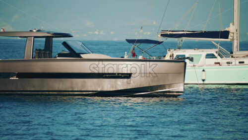 Video - Side view of a sleek metallic yacht reflecting sunlight on calm blue water