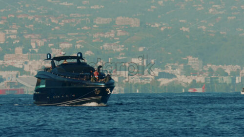 Video - Cannes, France - October 16, 2025: Elegant black yacht sailing across calm sea with a scenic coastal city backdrop