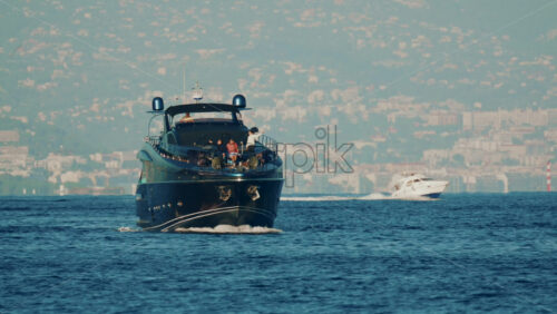 Video - Cannes, France - October 16, 2025: Elegant black yacht sailing across calm sea with a scenic coastal city backdrop