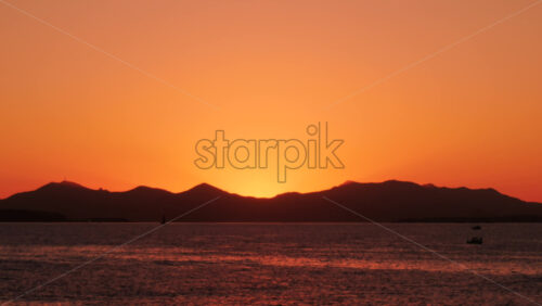 Video - Beautiful orange sunset behind mountain silhouettes over calm sea water