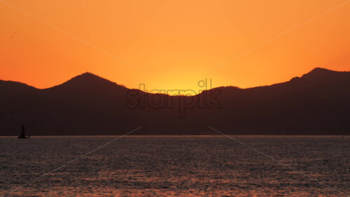 Video - Beautiful orange sunset behind mountain silhouettes over calm sea water