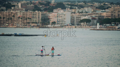 Video - Two people paddleboarding together near a coastal city with modern buildings