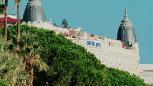 Video - Cannes, France - October 4, 2025: Elegant view of the Carlton hotel surrounded by lush green palm trees under clear blue sky