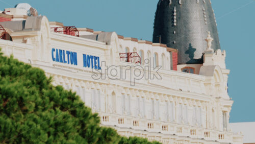 Video - Cannes, France - October 4, 2025: Elegant view of the Carlton hotel surrounded by lush green palm trees under clear blue sky