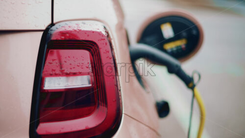 Video - Close up of a pink, electric car charging outdoors under rain