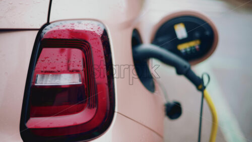 Video - Close up of a pink, electric car charging outdoors under rain