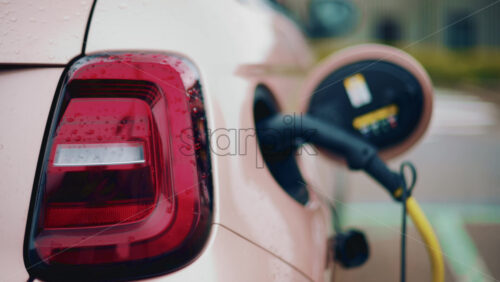 Video - Close up of a pink, electric car charging outdoors under rain
