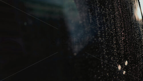 Video - Close up of raindrops on a glass window, softly illuminated by blurred bokeh lights in the background