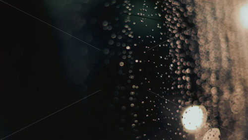 Video - Close up of raindrops on a glass window, softly illuminated by blurred bokeh lights in the background