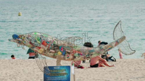 Video - Cannes, France - October 4, 2025: Metal dolphin sculpture filled with plastic waste displayed on a sandy beach by the sea, raising awareness about ocean pollution