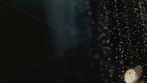 Video - Close up of raindrops on a glass window, softly illuminated by blurred bokeh lights in the background