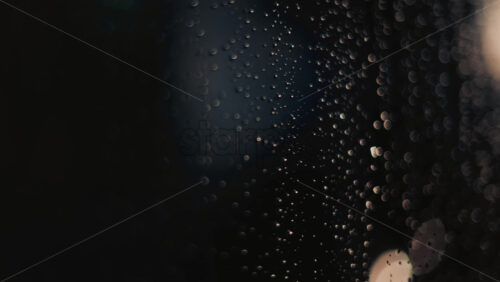 Video - Close up of raindrops on a glass window, softly illuminated by blurred bokeh lights in the background
