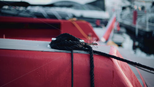Video - Close up of a red boat moored at a marina, with black rope coiled neatly on the deck