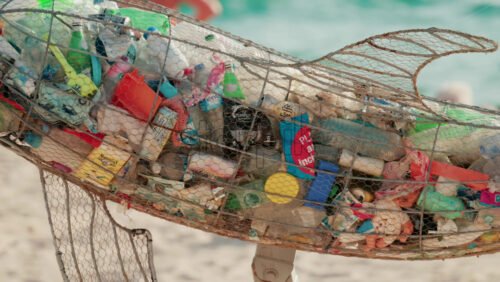 Video - Cannes, France - October 4, 2025: Metal dolphin sculpture filled with plastic waste displayed on a sandy beach by the sea, raising awareness about ocean pollution
