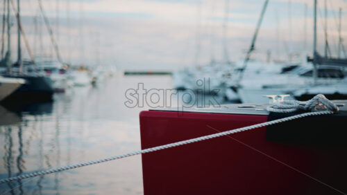 Video - Peaceful marina view showing a red boat tied with white ropes, surrounded by yachts on calm water