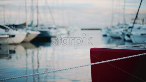 Video - Peaceful marina view showing a red boat tied with white ropes, surrounded by yachts on calm water