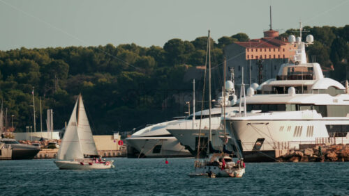 Video - Sailboats and luxury yachts anchored in Cannes harbor with clear blue water and trees in the background