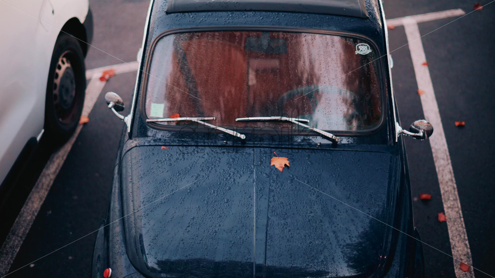Video - Cannes, France - October 20, 2025: Aerial view of a classic blue car covered in raindrops, parked in an urban lot
