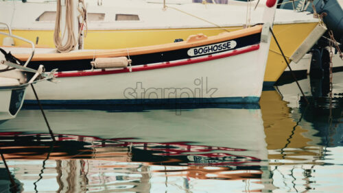 Video - Close up of a small boat with yellow and red accents reflecting beautifully on still marina water