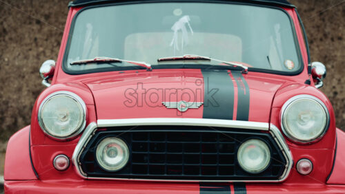 Video - Cannes, France - October 20, 2025: Frontal view of a vintage red Mini Cooper with black stripes, parked in front of a textured wall