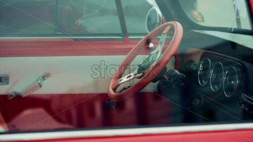 Video - Close up of a vintage car interior shot through the window, focusing on the red steering wheel and dashboard