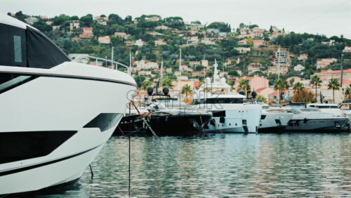 Video - Luxury yachts moored in a calm marina with a scenic hillside town in the background