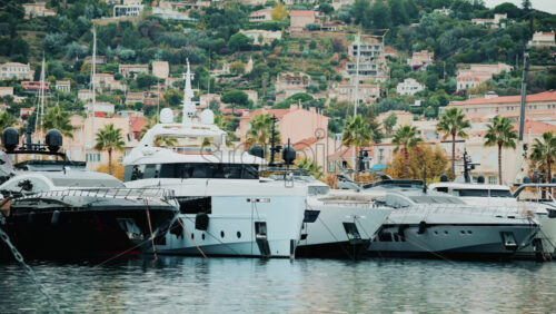 Video - Panoramic view of superyachts lined up in a marina, framed by palm trees and pastel houses on the hillside